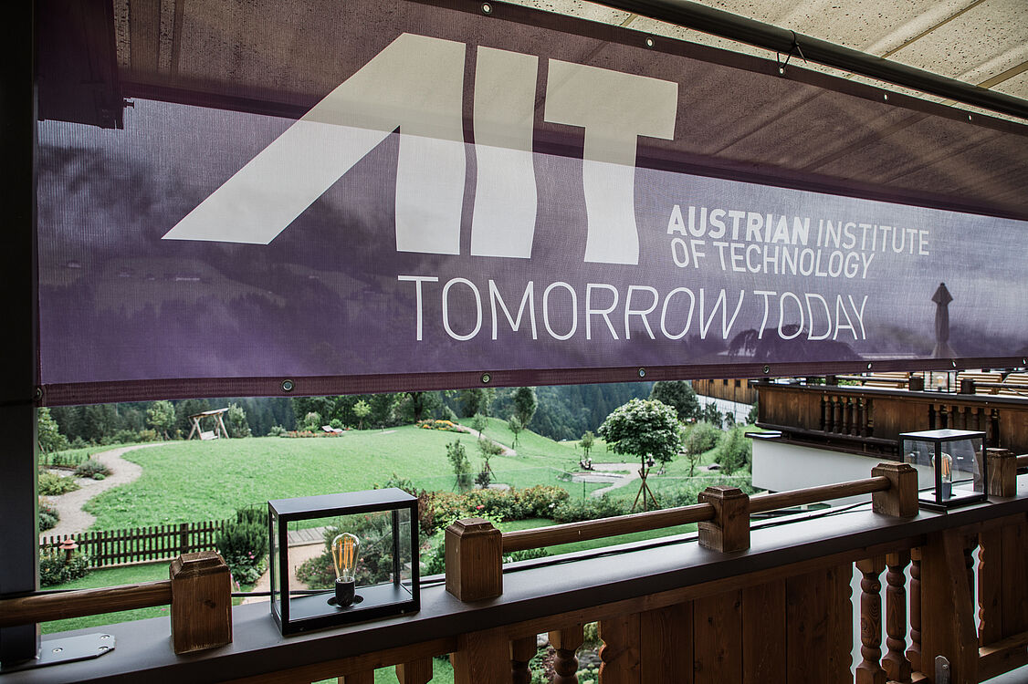 Ein Banner mit AIT-Aufschrift, ein Garten im Hintergrund