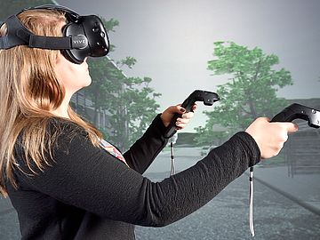 [Translate to English:] Auf dem Bild sieht man eine Frau mit VR-Brille und Controllern in der Hand.