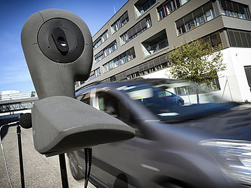 artificial head with microphone on the sidewalk and a car driving by