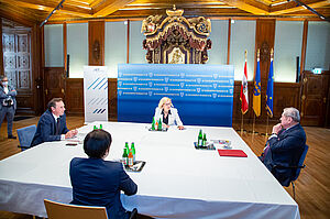 the four participants of the appointment sit at a large distance around a table in conversation in an impressive setting